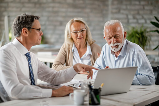 Mature couple and insurance agent using computer during consultations in the office.